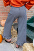 A person wearing wide-leg black and white gingham pants with ruffled hems, paired with an orange sweatshirt and black flats, standing outdoors near hay bales and pumpkins.