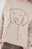 A close-up of a woman wearing a beige knit sweater with a simple brown line drawing of a dog on the front.