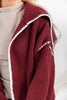 Close-up of a woman wearing a burgundy ribbed knit cardigan with white contrast trim over a light beige top.