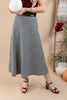 A woman models a black and white gingham plaid midi skirt with a black waistband, paired with burgundy heeled sandals and holding a white pumpkin against a warm beige background.
