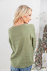 A woman from the back wearing an olive green knit sweater with horizontal textured stripes.