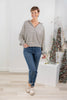 A woman modeling a long-sleeve striped V-neck top with blue jeans and beige shoes.