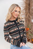 A blonde woman wearing a long-sleeve knit cardigan with a brown, beige, and black Fair Isle pattern, paired with light blue jeans.