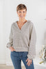 A woman modeling a cream and black horizontally striped long-sleeve top with a split V-neck, paired with blue jeans.