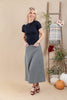 A woman modeling a black short-sleeve mock neck top and a black and white gingham check midi skirt, standing in a studio with a beige background, a wooden ladder decorated with a plaid throw and flowers, and pumpkins on the floor.