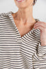 Close up of a woman wearing a cream and black horizontally striped long-sleeve top with a split V-neck.