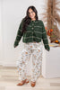 A woman modeling a dark green knit cardigan with thin cream stripes and white floral pants.