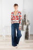 A woman wearing a cream-colored cardigan with a vibrant red and black floral pattern, paired with blue jeans.