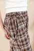 Close-up of a person wearing brown and white plaid drawstring pants with a white textured top, against a soft beige background.