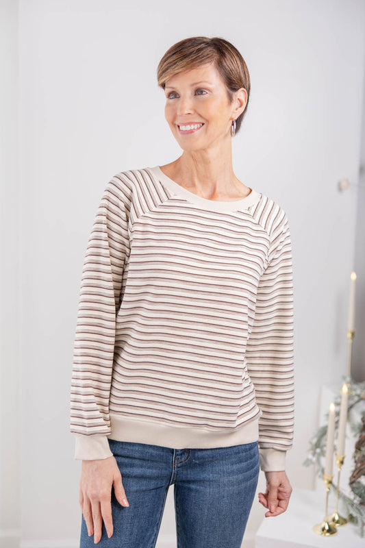 A woman wearing a beige and brown horizontally striped long-sleeve sweater with a crew neck.
