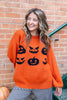 A woman wearing a long balloon sleeve, orange crew neck sweater with a black jack-o'-lantern graphics, paired with black and white gingham ruffled pants as she holds a jack-o-lantern.