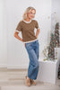 A woman wearing a brown short-sleeve knit top with white polka dots and cream ruffle trim at the collar, cuffs, and hem, paired with jeans.