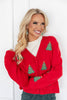 A woman wearing a bright red knit cardigan with green Christmas tree motifs and a white top.