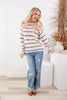 A woman crewneck sweater with horizontal stripes in orange, green, purple, and blue on an off-white base paired with distressed light-wash jeans and brown pointed-toe flats.