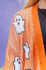 Close-up of a person wearing an orange knit cardigan with white vertical stripes and white sequin ghost appliqués outlined in black, over a black top against a purple background.
