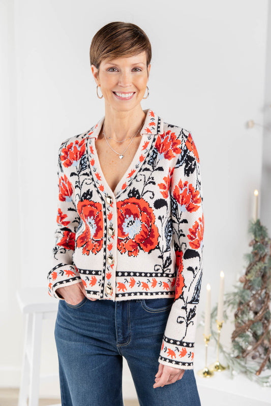 A woman wearing a cream-colored cardigan with a vibrant red and black floral pattern and gold buttons.