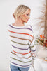A woman wearing a white knit sweater with horizontal stripes in purple, orange, green, and brown, shown from a three-quarter back view.