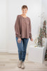 A woman modeling a brown long-sleeve henley top with blue jeans and beige ankle boots.