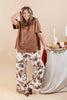 A woman modeling a brown faux suede short-sleeve top and brown-and-white cow-print wide-leg pants, standing next to a decorated table with candles and a pie against a beige studio background.