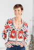 A woman wearing a cream-colored collared cardigan with a vibrant red and black floral pattern and gold buttons.