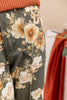 Close-up of a pair of dark olive green denim pants featuring a large cream and orange floral print, styled with an orange ribbed knit top.