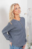 A blonde woman wearing a slate blue-gray ribbed henley top with brown buttons.