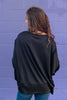A woman from behind wearing a black crewneck sweatshirt standing against a purple brick wall.