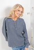 A woman wearing a gray-blue waffle knit long-sleeve henley top with blue jeans.
