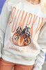 A close-up of a person wearing a cream-colored sweatshirt with a 'Pumpkin Season' graphic featuring an orange pumpkin with a leopard-print bow, paired with rust-colored pants.