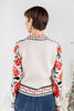 A woman from behind wearing a cream-colored collared cardigan with a vibrant red and black floral pattern.