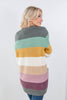 A woman wearing a fuzzy knit sweater with horizontal stripes in gray, mint green, mustard yellow, cream, beige, pink, and purple, shown from a back-three-quarter view against a light gray studio background.
