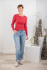 A woman modeling a red long-sleeve henley top and light blue distressed jeans.