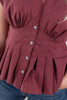 Close-up of a sleeveless burgundy top with a gathered waist, buttoned front, and peplum-style flared hem, worn with blue jeans.