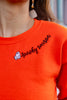 Close up of embroidered ghost and cursive "spooky season" text along neckline of bright orange sweatshirt