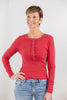 A woman modeling a red long-sleeve henley top with button placket and light blue jeans.