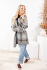 A woman modeling a gray and brown plaid knit cardigan over a dark top, paired with light blue jeans and brown slip-on shoes.