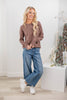 A woman modeling a brown long-sleeve henley shirt and blue wide-leg jeans.