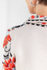 A close up of a woman from behind wearing a cream-colored collared cardigan with a vibrant red and black floral pattern.