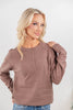 A woman wearing a long-sleeve henley-style knit top in a muted taupe-brown color, paired with blue jeans.