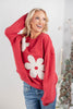 A woman wearing a red crewneck sweatshirt with large white flower appliques.