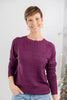 A woman wearing a long-sleeve crewneck sweater in a deep plum purple color, paired with light blue jeans.