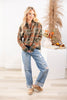A woman models a long-sleeve plaid half zip jacket in rust orange, olive green, and black, paired with distressed light-wash blue jeans and tan loafers.
