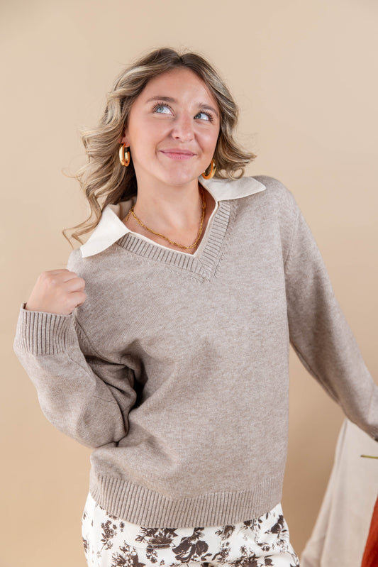 A woman wearing a light taupe knit sweater with a contrasting white collar, posing against a solid beige background.