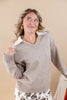 A woman wearing a light taupe knit sweater with a contrasting white collar, posing against a solid beige background.