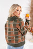 A woman wearing a fuzzy knit plaid sweater in earthy green, rust orange, and beige tones from the back.