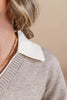 Close-up of a woman wearing a beige knit sweater with a contrasting white pointed collar, against a warm beige background.