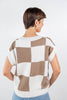 A woman from behind wearing a short-sleeve knit sweater with a beige and off-white checkered pattern.