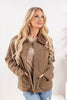 A woman modeling a tan corduroy-like button-up jacket with a brown collar, worn with blue jeans.