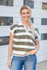 A woman smiling in front of a white garage wall, wearing a short-sleeve knit polo shirt with horizontal olive green and white stripes, a white collar, and a split V-neck.