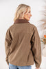 A woman shown from the back wearing a brown corduroy-like jacket with a contrasting darker brown collar, paired with blue jeans.